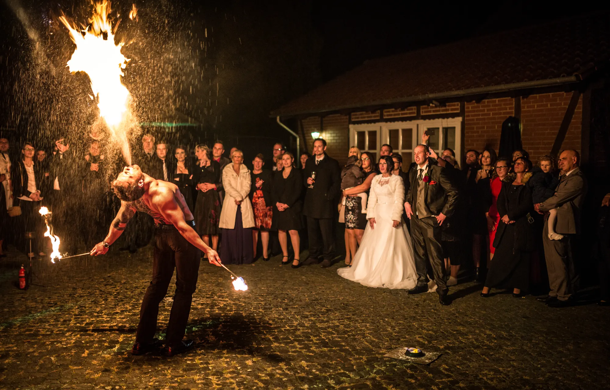 Feuerkünstler spuckt Feuer im Regen, Brautpaar und Hochzeitsgäste schauen zu