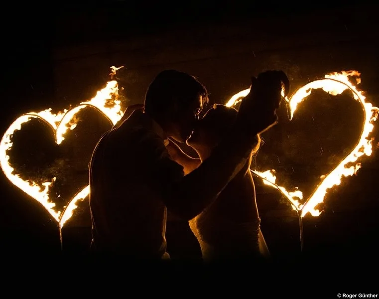 Brautpaar küsst sich im Schein zweier brennender Flammenherzen